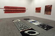 Works by Michael Reed: on floor, Runners for the Corridors of Power, Dilana Rugs , digital dye on nylon, on left wall, 15 screenprinted cotton bandages, on right, Three in One, screenprint and photocopy on acetate, and Maximum Radius, screenprint /acetate