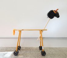PĀNiA!, Orange Builder’s Pony With Ear Bonnet or Protective Muff, 2025 Folding saw horse, hobby horse head, customised thermal pvc glove, dowel, glue, faux leather bridle, hand duster, stroller wheels, fake eyelashes, band aids, bandage, fixings, sound