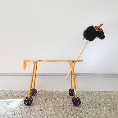 PĀNiA!, Orange Builder’s Pony With Ear Bonnet or Protective Muff, 2025, Folding saw horse, hobby horse head, customised thermal pvc glove, dowel, glue, faux leather bridle, hand duster, stroller wheels, fake eyelashes, band aids, bandage, fixings, sound